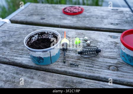 Un plan rapproché d'équipement de pêche, comprenant une tasse d'appât, un flotteur et des poids, reposant sur une table de pique-nique en bois usé près de l'eau. Perfe Banque D'Images