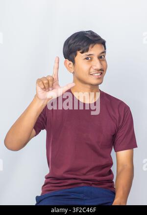 Jeune mannequin indonésien élégant pointant vers le haut avec un sourire enthousiaste dans le studio. Banque D'Images