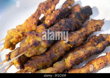 Close-up de brochettes de poulet satay malaisiennes fraîchement grillées montrant des bords carbonisés et une texture assaisonnée sur une assiette blanche. Banque D'Images