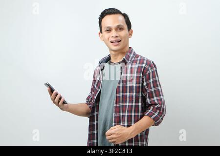 Homme indonésien asiatique heureux tenant un smartphone. Sur fond isolé Banque D'Images
