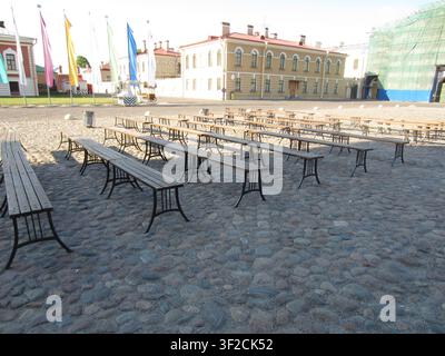 Des rangées de bancs et de tables en bois se dressent sur une cour pavée à l'intérieur de la forteresse Pierre-et-Paul à Saint-Pétersbourg, en Russie. Banque D'Images