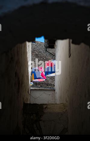 Szentendre, Hongrie - 04 juillet 2026 : Vue à travers une arche de pierre sombre vers des abat-jour colorés suspendus et un toit de tuiles dans une ruelle historique étroite. Banque D'Images