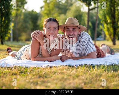 Un couple heureux se détend sur une couverture de pique-nique dans un parc paisible, profitant d'un après-midi chaud ensemble. Banque D'Images