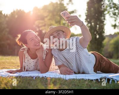 Couple multiculturel passant du temps ensemble dans un parc en été. Ils utilisent un smartphone et prennent un selfie. Banque D'Images
