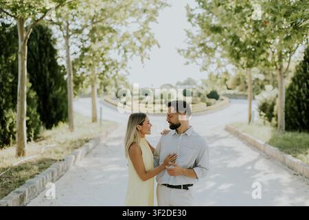 Dans un jardin serein rempli de verdure, un couple partage une étreinte tendre, se délectant de la chaleur du soleil. L'atmosphère est joyeuse et intime. Banque D'Images