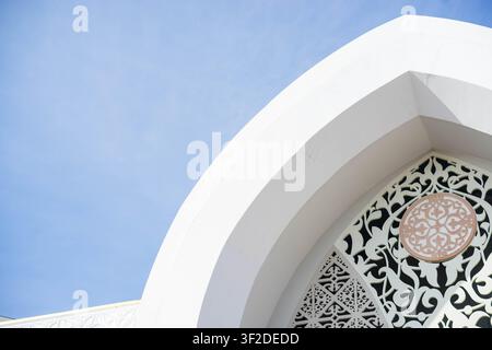 Vue détaillée d'une élégante arche architecturale blanche présentant des motifs géométriques islamiques complexes sous un ciel clair Banque D'Images