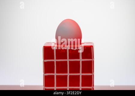 Nature morte conceptuelle audacieuse avec un cube grille rouge vif et un œuf teinté rouge sur fond blanc. Composition minimale à contraste élevé, photographie graphique en studio Banque D'Images