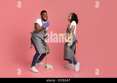 Concept de service d'entretien joyeux. Couple africain joyeux de nettoyeurs ayant du plaisir pendant les tâches Banque D'Images