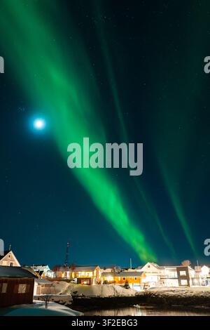 Affichage époustouflant des aurores boréales illuminant un village enneigé des îles Lofoten, en Norvège. L'aurora vibrante danse au-dessus du paysage hivernal, cre Banque D'Images