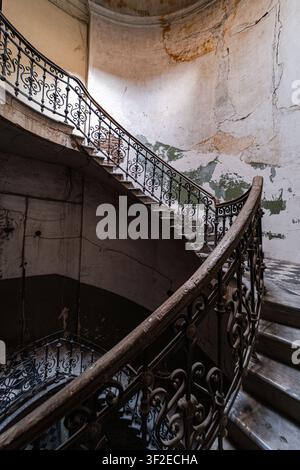 Un escalier en fer forgé complexe dans un bâtiment abandonné, mettant en valeur de belles caractéristiques architecturales. Les murs sont vieillots et écaillés, ajoutant une se Banque D'Images