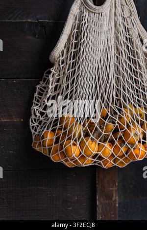 Fruits de loquat mûrs dans un sac de courses réutilisable en filet de coton accroché contre un fond en bois rustique sombre, mettant en valeur des produits frais de saison, des vitamines Banque D'Images