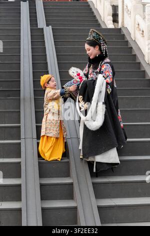 Femme et enfant chinois traditionnels en costume ethnique orné sur un escalier à Pékin, en Chine, partageant un bouquet dans une scène de voyage culturel avec héritage Banque D'Images
