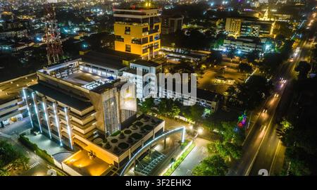Vue aérienne d'un complexe de bâtiments de bureaux modernes illuminé la nuit avec des traînées de lumière provenant de la circulation sur la route adjacente au Ghana. Banque D'Images