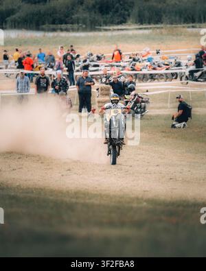 Angleterre, Royaume-Uni - 04 juillet 2023 : Vue d'un pilote de motocross effectuant un wheelie sur une moto tout-terrain, soulevant de la poussière sur un champ herbeux avec des spectateu Banque D'Images