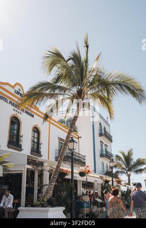 Las Palmas, Espagne - 17 juillet 2025 : Vue de l'hôtel Puerto de Mogan avec des palmiers, des bâtiments blancs aux ornements jaunes et bleus, et des gens marchant sur un su Banque D'Images