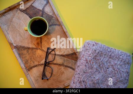 Composition chaleureuse avec une tasse de café, des verres et un vêtement tricoté sur un fon-de jaune. Banque D'Images