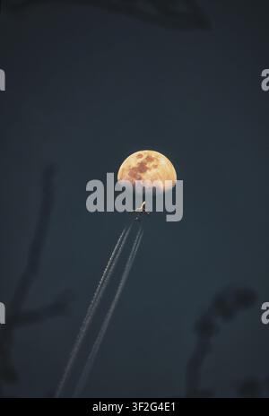 Vue aérienne d'un avion de ligne volant devant une lune brillante laissant de longues traînées dans le ciel nocturne au-dessus de Shanghai, Shanghai, Chine Banque D'Images
