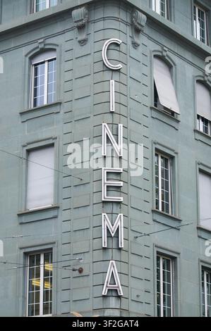 Panneau néon vertical vintage portant l'inscription CINEMA monté au coin d'une façade de bâtiment classique gris-bleu. La structure architecturale présente une symétrie Banque D'Images