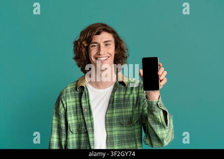 Joyeux adolescent caucasien montrant un téléphone mobile avec écran vide sur fond couleur, espace pour votre design Banque D'Images