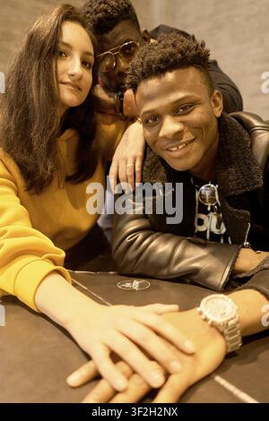 Sourire d'amis à la mode passant du temps ensemble à une table avec les mains les unes au-dessus des autres en signe d'accord et de soutien mutuel, attitude cool Banque D'Images