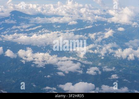 Survolant les sommets des montagnes et les vallées avec des nuages cumulus blancs dispersés, observant le vaste paysage verdoyant depuis une perspective aérienne pendant la journée Banque D'Images