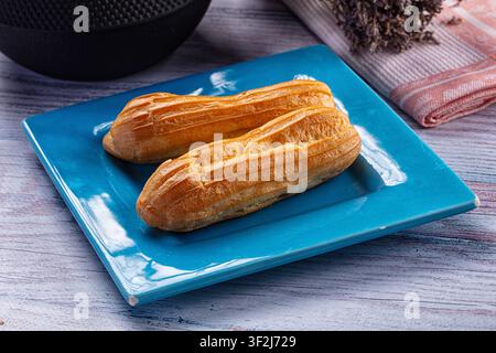 Choux dorés sur une assiette carrée bleue brillante. Surface en bois rustique avec un éclairage doux aux tons chauds. Composition alimentaire minimaliste avec une serviette texturée Banque D'Images