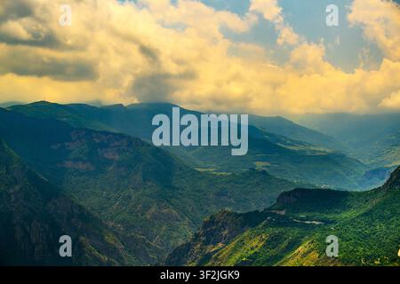 La lumière du soleil perce les nuages au-dessus des vallées montagneuses. Des collines ondulantes recouvertes d'une végétation verte. La brume s'enroule entre les crêtes Banque D'Images