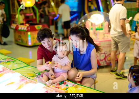 Deux femmes et un enfant sont assis à côté de jouets colorés et de jeux illuminés dans une arcade animée. Banque D'Images