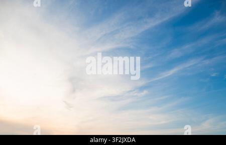 Un ciel serein et vaste avec des nuages cirrus doux et effilochés s'étendant sur un horizon bleu vif, se transformant en une lueur chaude et dorée à la Banque D'Images