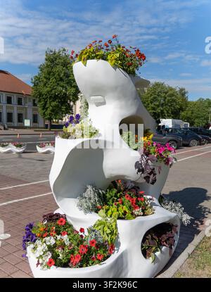 Fleurs de pétunia colorées dans des bacs à fleurs blancs modernes en bord de rue, avec un bâtiment historique flou, un panneau de signalisation et un arrière-plan estival de ville. Banque D'Images