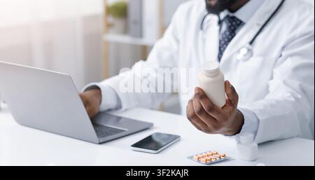 Médecin tenant bouteille avec des pilules, en utilisant un ordinateur portable Banque D'Images