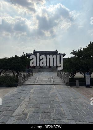 25 juillet 2025, Séoul, Corée du Sud – Cour pavée de pierre au palais de Gyeongbokgung avec toit de pavillon hanok traditionnel et nuages d'été dramatiques. Banque D'Images