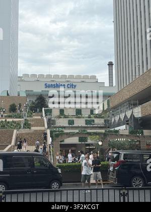 11 août 2025, Toshima, Tokyo, Japon – Façade du complexe Sunshine City avec des piétons et des véhicules sur une rue animée du quartier d’Ikebukuro, Tokyo. Banque D'Images