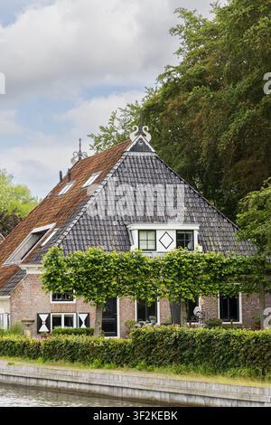 Maison de canal historique charmante à Sloten, Friesland, Pays-Bas présentant une architecture traditionnelle de ferme néerlandaise, un toit de tuiles, des lucarnes et un t Banque D'Images