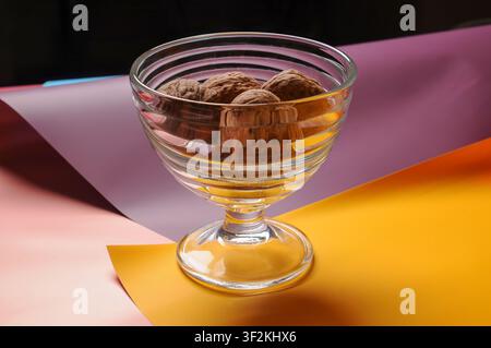 Une vue rapprochée de confiseries au chocolat noir présentées dans un plat en verre décoratif, posées sur un fond de papier vibrant et stratifié Banque D'Images