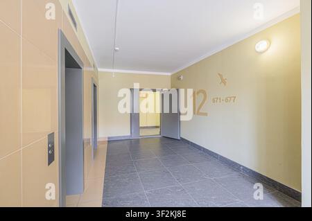 Vue intérieure du couloir d'un immeuble d'appartements avec des ascenseurs d'un côté et des marquages des numéros d'appartement sur le mur Banque D'Images