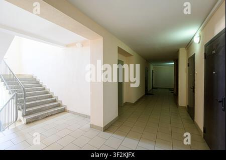 Une prise intérieure d'un couloir et d'un escalier dans un immeuble résidentiel. Les murs sont beige clair et le sol est carrelé Banque D'Images