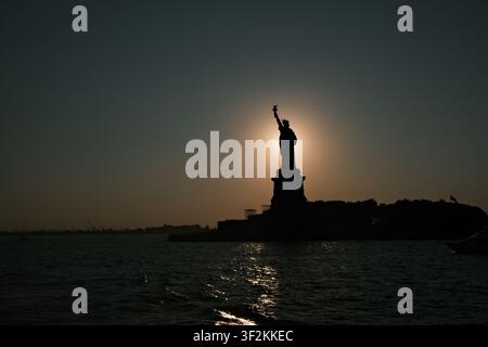 Liberté : le soleil se couche derrière une icône de la liberté dans le port de New York Banque D'Images