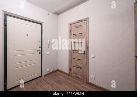 Plan intérieur montrant un couloir avec deux portes, l'une blanche avec un cadre noir et l'autre couleur bois. Le sol est composé de planches à veinures de bois Banque D'Images