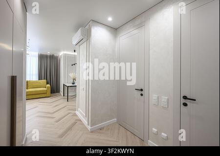 intérieur moderne avec des murs blancs, un parquet en bois et des portes blanches. Un aperçu d'un canapé jaune dans le salon est visible Banque D'Images