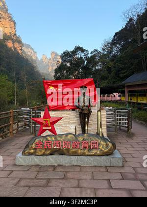 5 novembre 2025, Wulingyuan, Zhangjiajie, Chine – Statue en bronze d’un soldat avec le drapeau rouge de l’Armée populaire de libération et monument de la base d’éducation militaire patriotique chinoise au milieu du paysage karstique. Banque D'Images