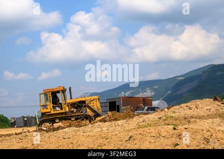 Bulldozer jaune déplace de la terre sur le chantier de construction. Paysage montagneux sous un ciel nuageux Banque D'Images
