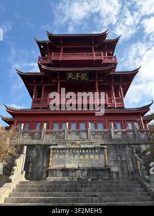 5 novembre 2025, Wulingyuan, Zhangjiajie, Chine – Vue en contre-plongée d’un pavillon chinois traditionnel à plusieurs pans, rouge et orné, avec une calligraphie dorée et un panneau d’inscription en pierre. Banque D'Images