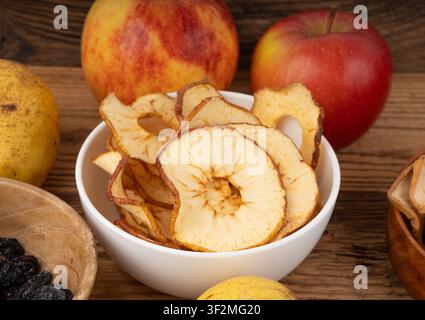 Tranches de pomme séchées sur table en bois. Chips de pomme séchés, en-cas de fruits sains dans un bol, anneaux gourmands déshydratés, chips de poire sucrée dénoyautées et croquantes sur un bac rustique Banque D'Images