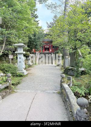 3 septembre 2025, Kanazawa, Japon – Lanternes en pierre traditionnelles et structure rouge d’un sanctuaire shintoïste entourés d’une végétation luxuriante à Kanazawa. Banque D'Images