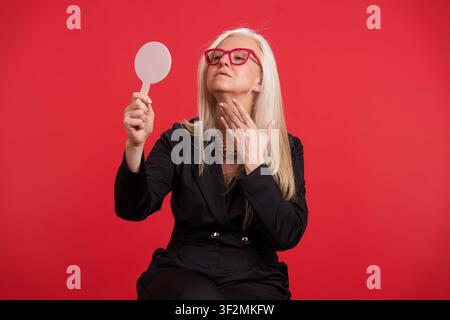 Femme mûre vérifiant la peau du cou dans le miroir pour l'anti-âge Banque D'Images