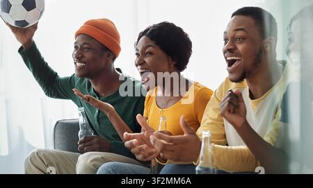 Groupe jeune afro-américain excité célébrant un match de football à la maison, souriant ensemble Banque D'Images