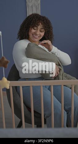 Femme berçant le bébé emmailloté, tapotant à la main la couverture tricotée par le berceau dans le bâtiment de la chambre de bébé, souriant à l'enfant ; tendresse. Banque D'Images