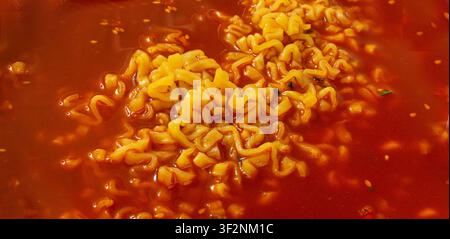 Soupe de nouilles épicée rouge à motif texturé. Fond de ramen au poivre de chili épicé, fond de pâtes coréennes épicées en gros plan et vue de dessus Banque D'Images