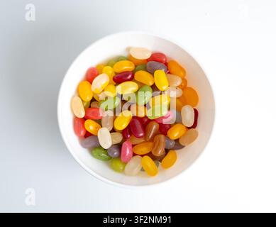 Pile de bonbons gélifiés en forme de haricots dans un bol isolé. Mâcher des pilules de confiture colorées, tas de gouttes de gelée, ensemble de bonbons en gelée sur fond blanc Banque D'Images